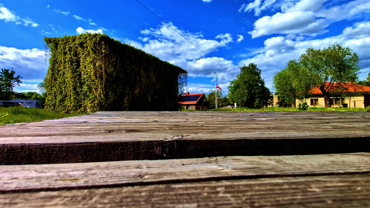 Low view of ivy-covered shed and wooden platform under blue sky with clouds