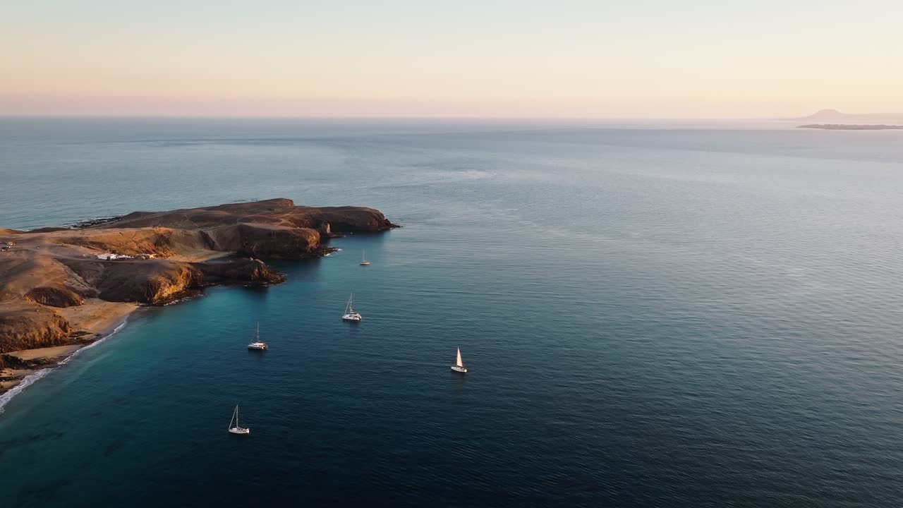 Stunning Drone Flight Over Lanzarote's Playa Mujeres with Sailboats and Fuerteventura in the Background During Beautiful Sunset