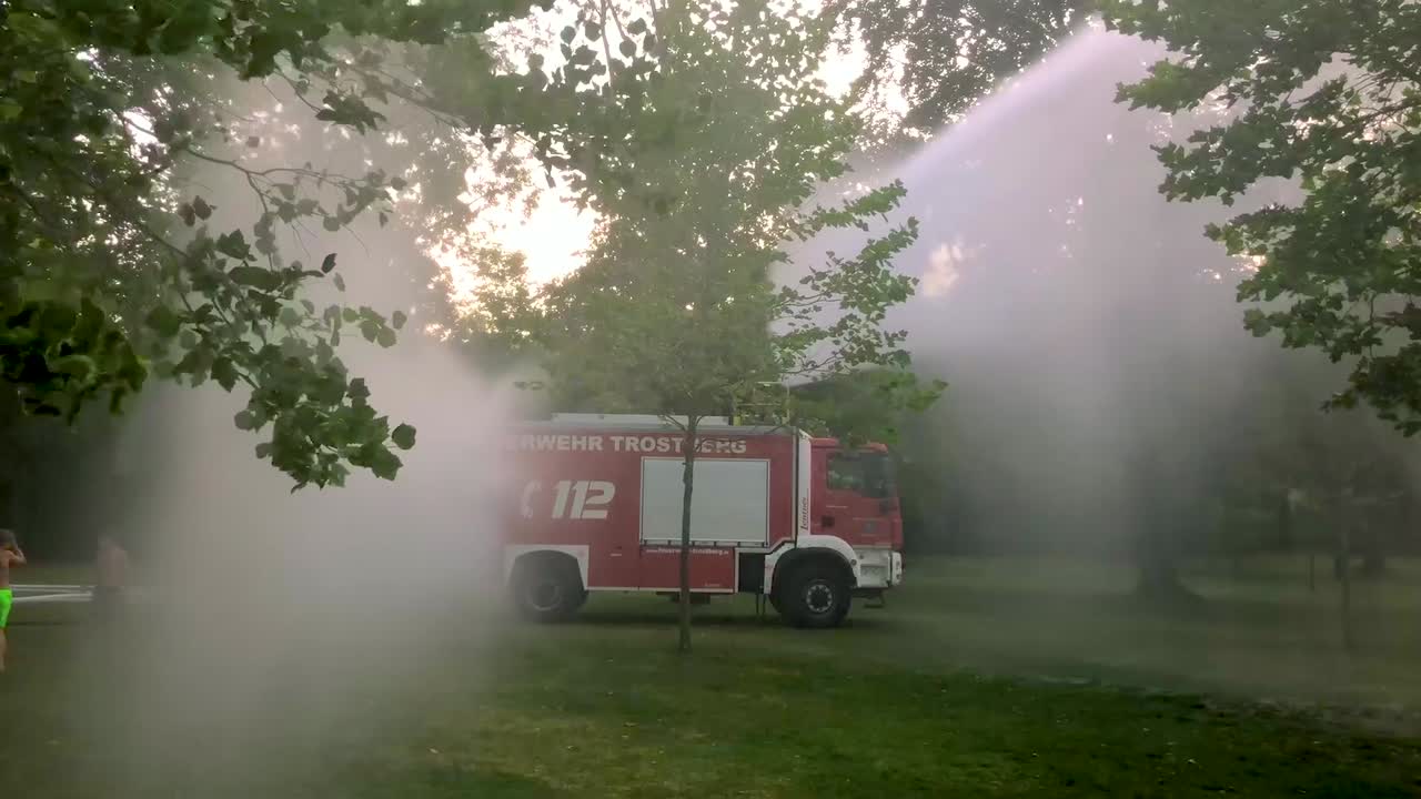 camión de bomberos alemán rociando agua para niños y árboles en un caluroso día de verano-2