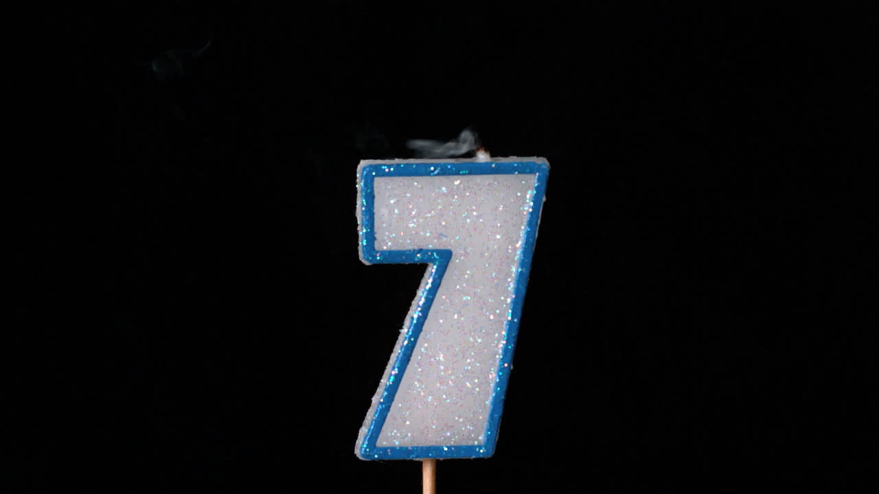 siete velas de cumpleaños parpadeando y apagándose sobre un fondo negro