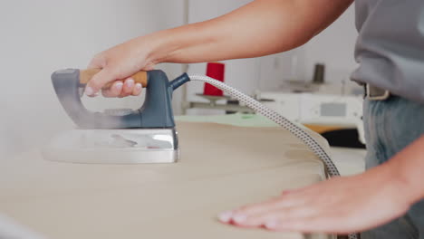 tailor ironing fabric on pressing table, focusing on neat finishing, removing wrinkles, ensuring crisp lines, using skillful approach, highlighting professional technique, achieving polished outcome