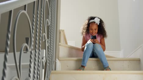 front view of happy black girl using mobile on stairs at comfortable home 4k