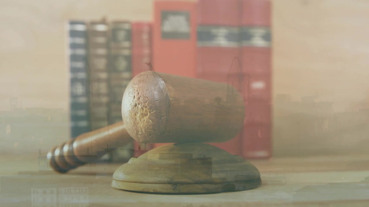 Cámara abriéndose sobre un mazo de juez entre libros de leyes, manteniéndose estable con iluminación cambiante mostrando grano