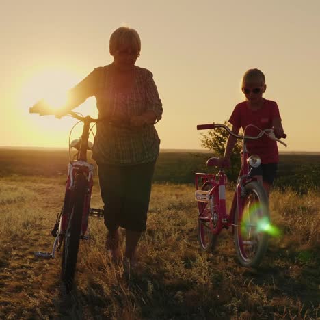 an elderly lady walks with her granddaughter bicycles at sunset