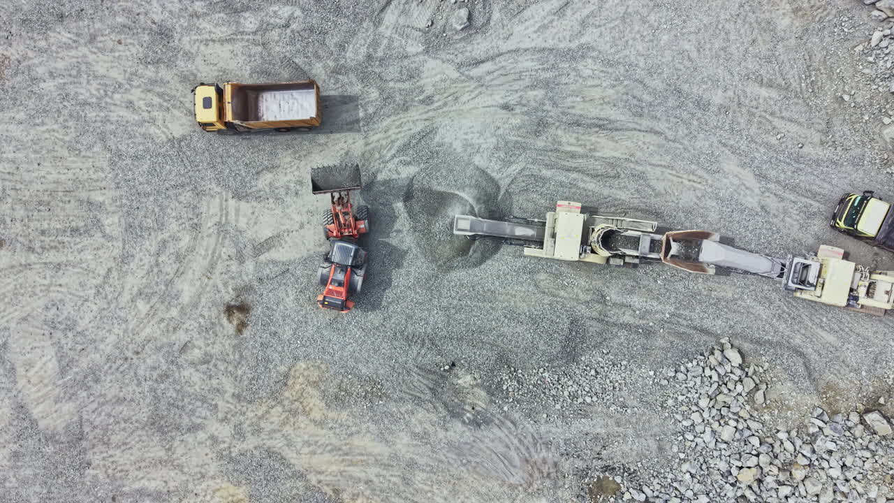 Workers operate heavy machinery in a granite quarry during daylight hours to extract stone for construction purposes