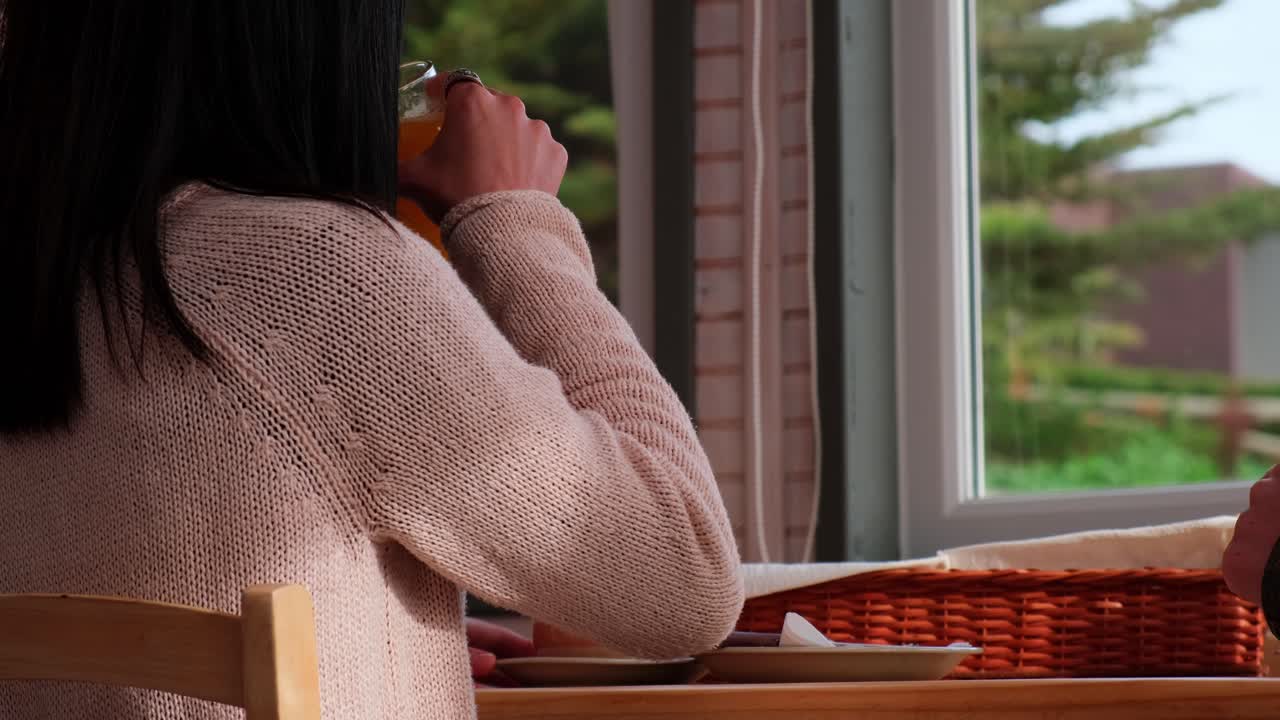 donna beve succo d'arancia mentre guarda attraverso la finestra un cipresso in una giornata nuvolosa nelle sue vacanze in cile pichilemu