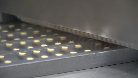 pharma laboratory conveyor belt moves round drug pills on machine, close up