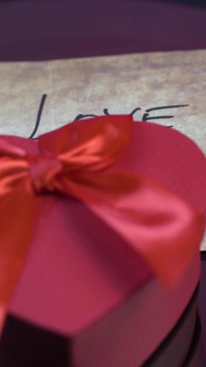 Visuale verticale, messaggio con scritto “Ti amo” e scatola regalo a forma di cuore rosso per San Valentino