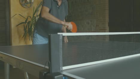 Un-Hombre-Está-Jugando-Al-Ping-Pong,-Disparado-Desde-Abajo,-Se-Puede-Ver-La-Red-Y-Detrás-De-Ella-Una-Persona-Golpeando-La-Pelota-Con-Una-Paleta-Roja