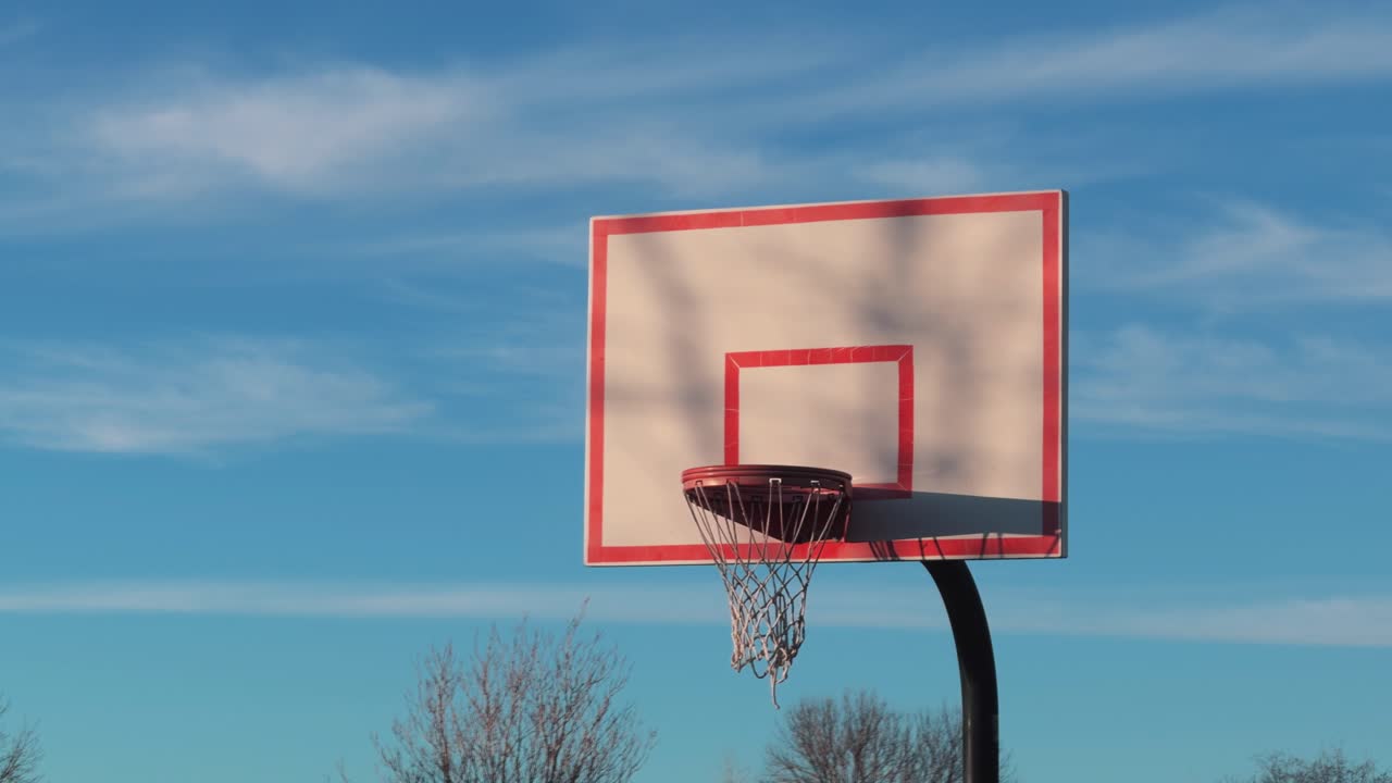 Inquadratura statica di un canestro da basket all'aperto in un parco pubblico sotto un cielo sereno