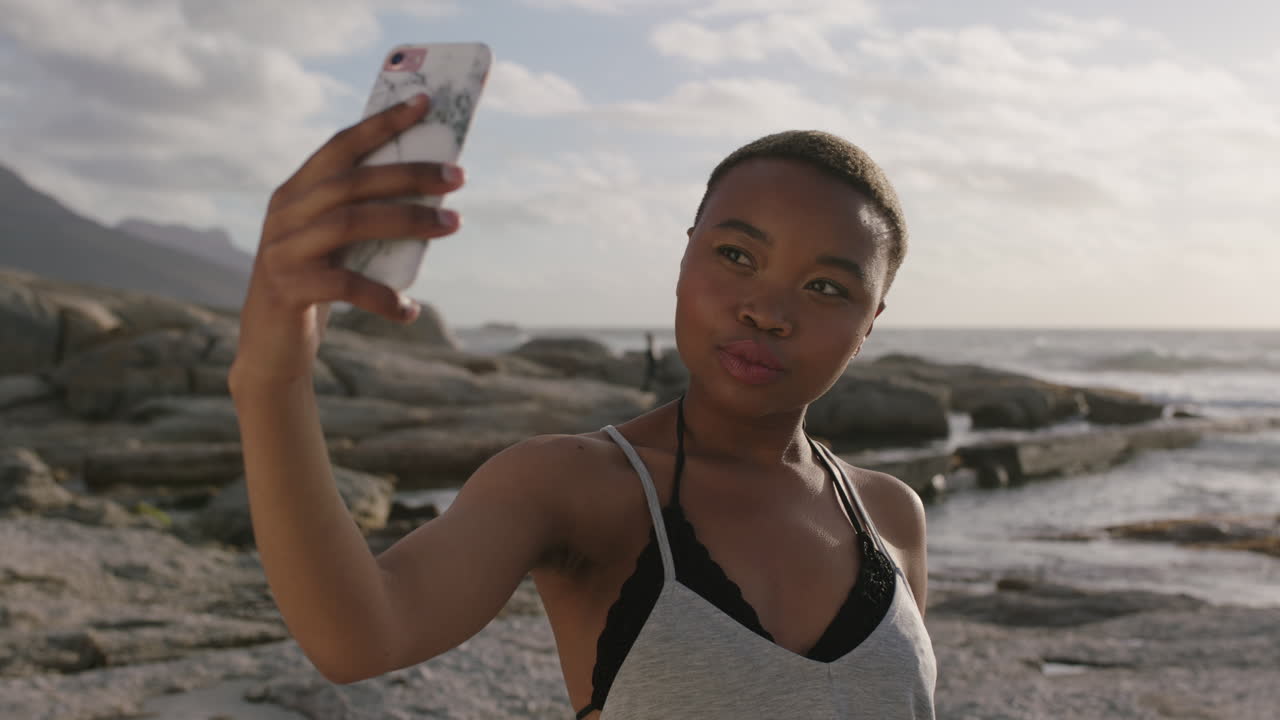retrato de una joven negra posando tomando una foto selfie en la playa usando el teléfono