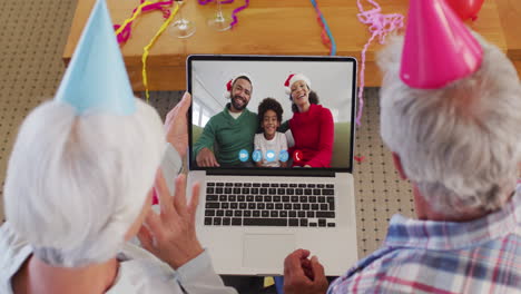 caucasian senior couple wearing party hats on laptop video chat during christmas at home