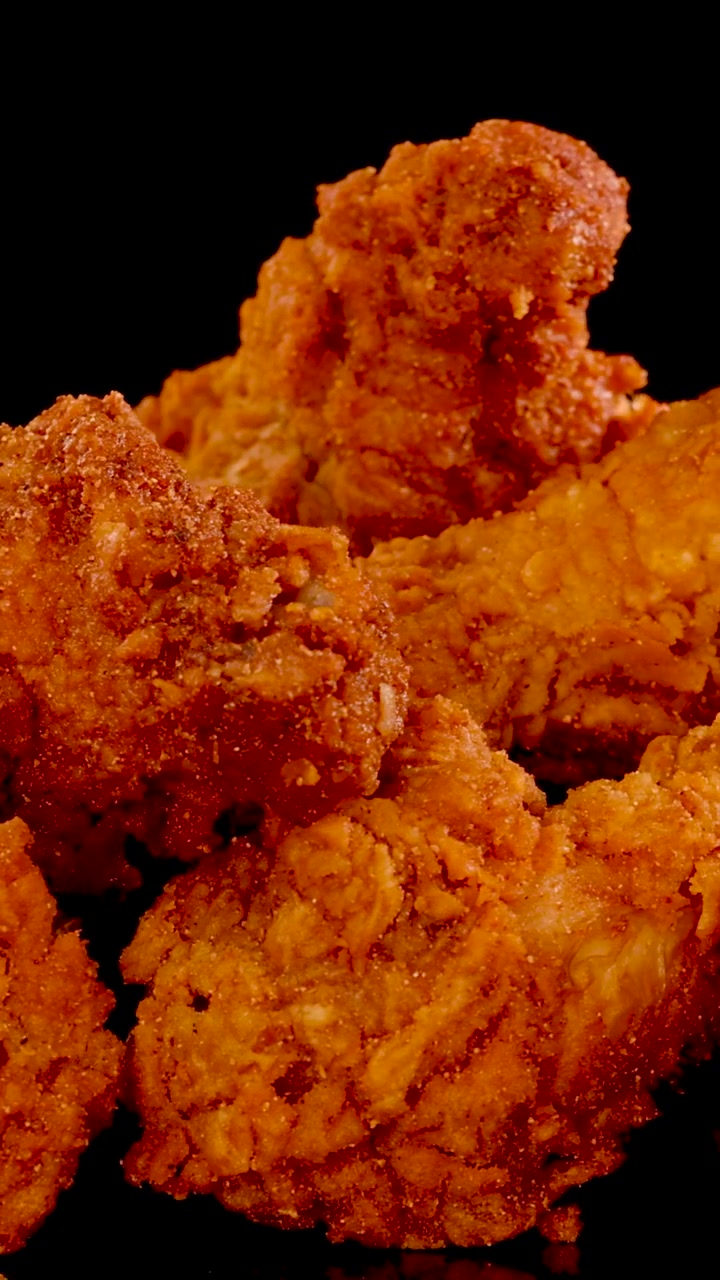 Ripresa macro verticale di pollo fritto dorato e condito che ruota su uno sfondo scuro.