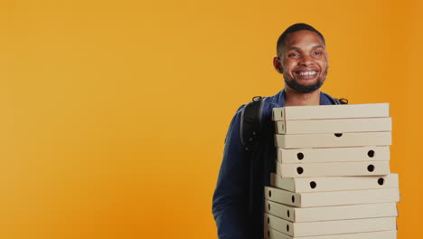 african american pizzeria deliveryman holding stack of pizza boxes