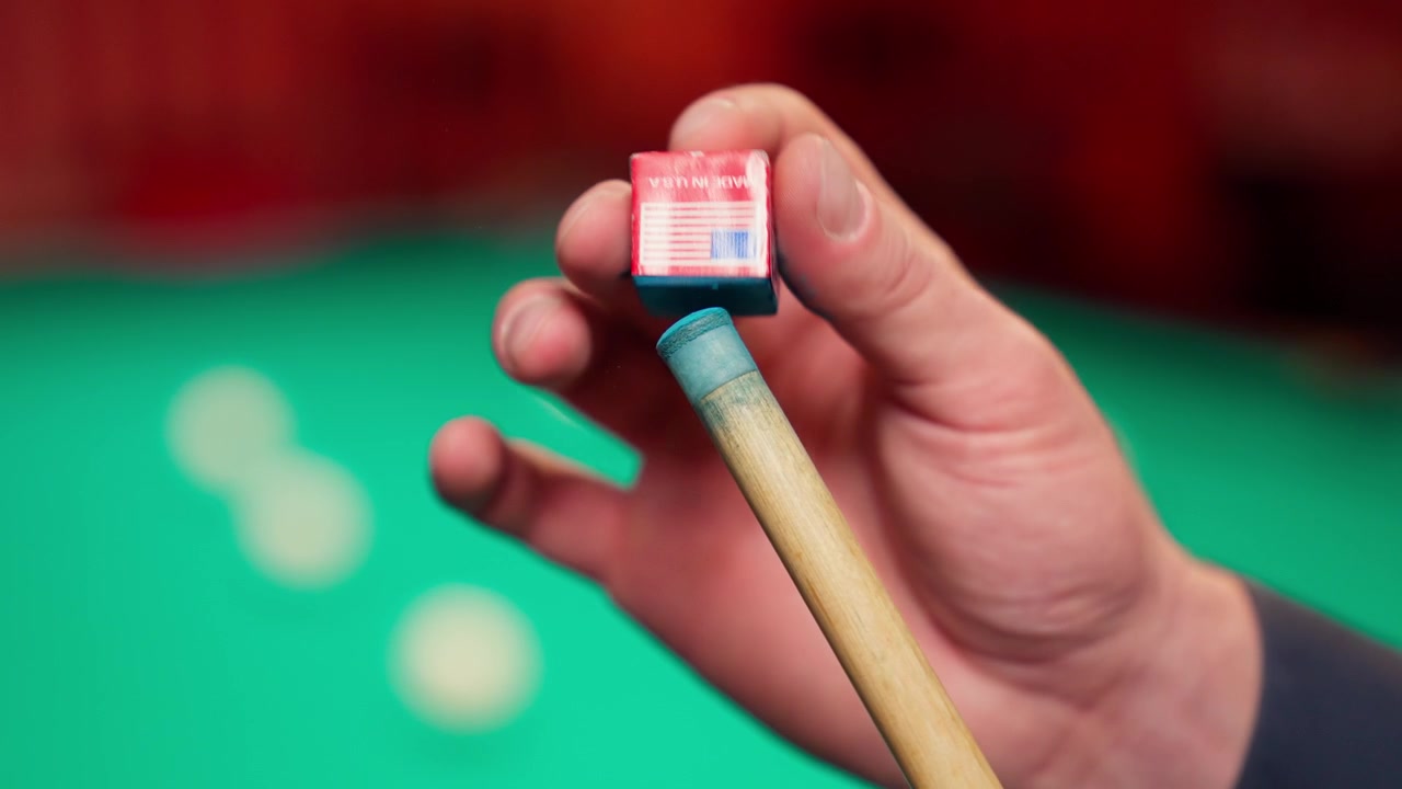 Primer plano de una mano aplicando tiza a la punta de un taco de billar
