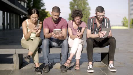 focused developers with digital devices sitting on bench