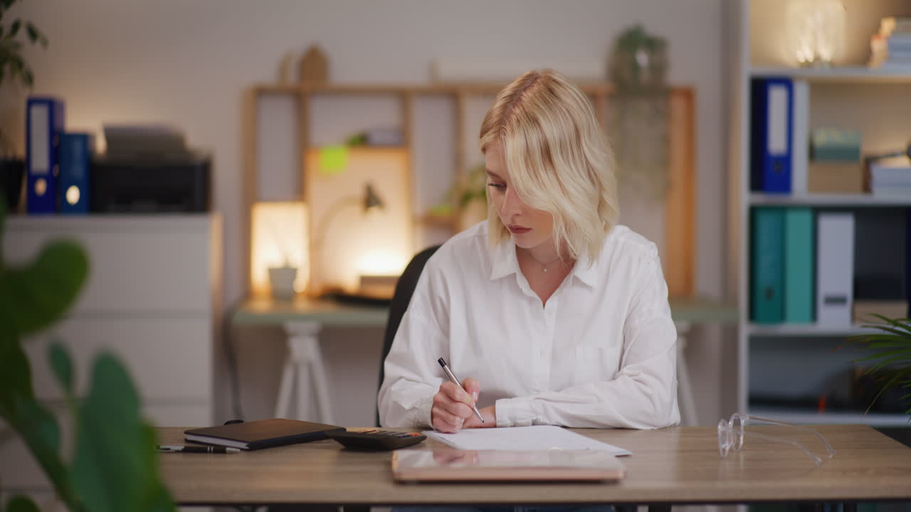 Überarbeitete Frau holt abends am Schreibtisch Arbeit nach