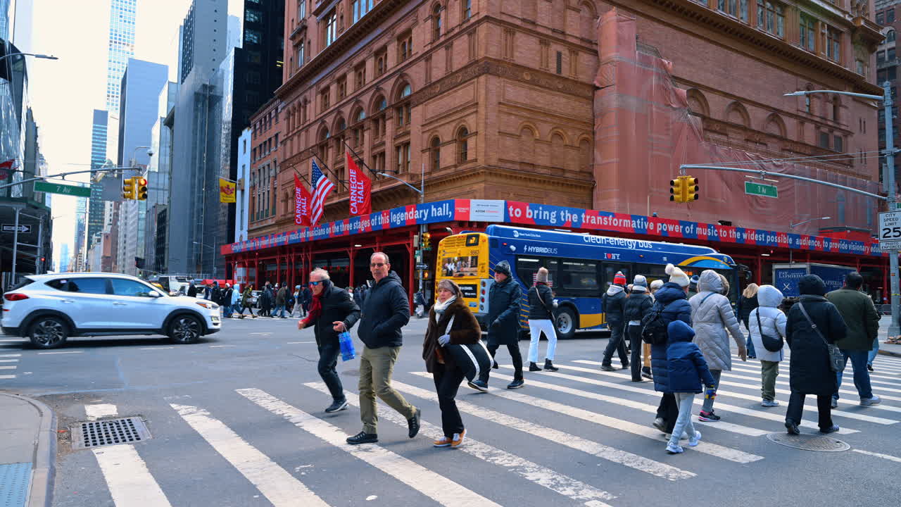 New York, USA, 2 March 2026: Pedestrians crossing 7th Avenue near Carnegie Hall in Manhattan. People using a crosswalk on 7th Avenue with a blue bus and Carnegie Hall building in New York City