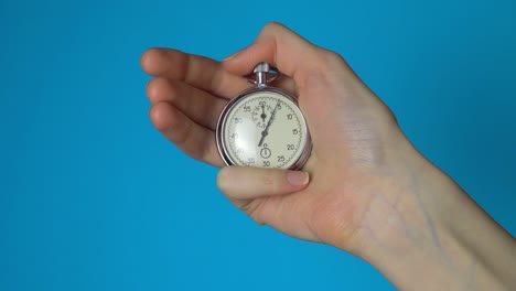 a woman's hand holds an analog stopwatch on a blue chromakey screen.