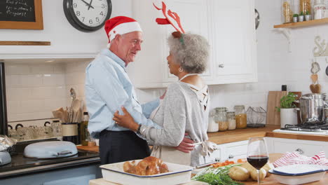 Liebevolles-älteres-Paar-Mit-Kostümgeweihen-Tanzt-In-Der-Küche,-Während-Es-Das-Weihnachtsessen-Zubereitet