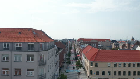 Bird's-eye-of-Torvegade,-one-of-Denmark's-longest-pedestrian-streets,-in-Esbjerg.-Forward-flight-through-downtown-of-the-city-with-characteristic-historical-brick-building-and-pedestrian-strolling