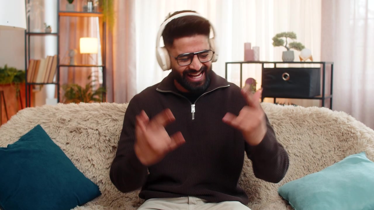 Un uomo indiano sorridente ascolta musica energica con le cuffie wireless e mostra un gesto rock'n'roll