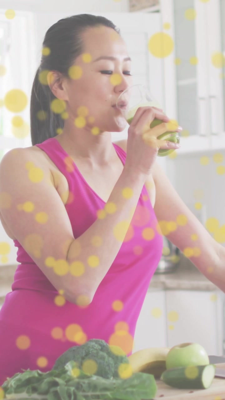 Video verticale: Donna che osserva, solleva un succo verde e lo sorseggia per la salute, con bokeh giallo intorno a lei.