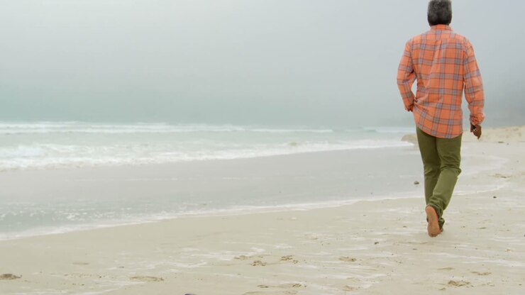 Rear view of active senior African American man with hand in pocket walking on the beach 4k