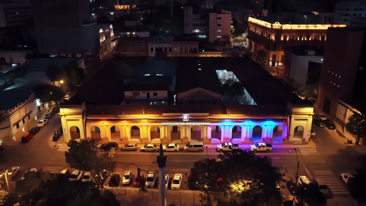 Dolly in aerial view of Comandancia de la Policía Nacional building, lit in yellow and blue. Asunción, Paraguay