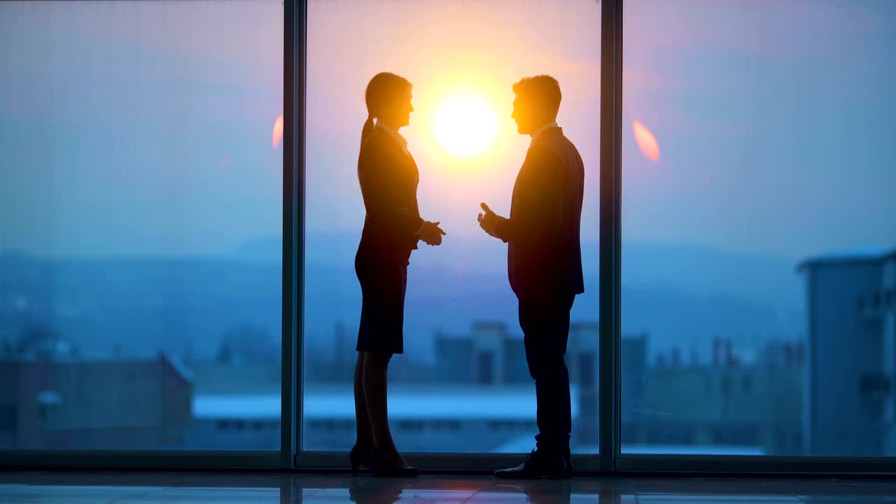 Un uomo e una donna che conversano vicino alla finestra panoramica con uno sfondo all'alba