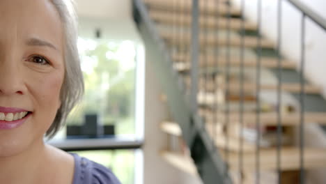smiling senior asian woman standing in modern home with staircase in background