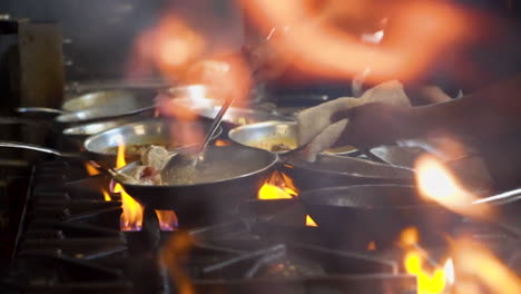 chef sautes dishes over flames in restaurant kitchen, foreground flare up from stove, cinematic slider slow motion hd