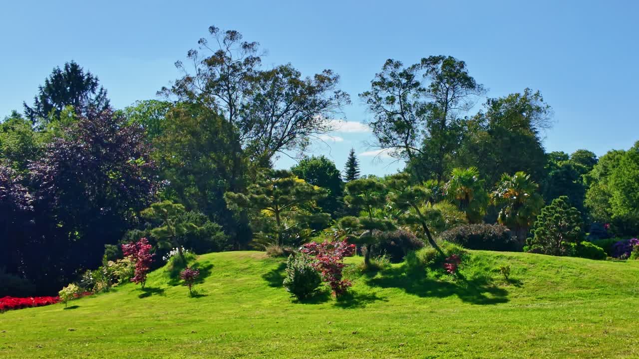 Blick auf einen gepflegten Rasenhügel, geschnittene Sträucher und Bäume unter einem klaren blauen Himmel im Botanischen Park Haute Bretagne