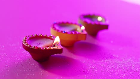 Close-up-of-burning-colourful-candles-celebrating-diwali-on-purple-background