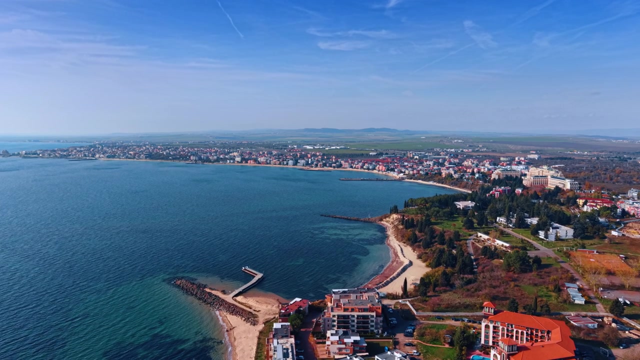 Vista aerea panoramica di una baia curva e di una città turistica costiera sul Mar Nero. Edifici del resort con tetti rossi costeggiano l'arco di una grande baia curva dove la costa sabbiosa incontra le calme acque blu del mare.