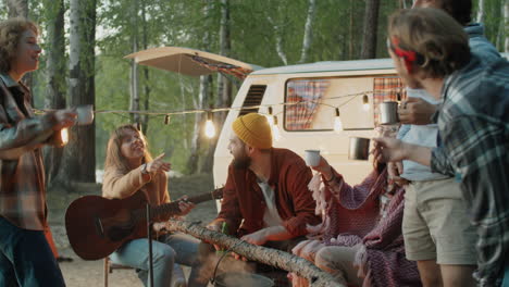 friends clinking drinks in toasts by campfire