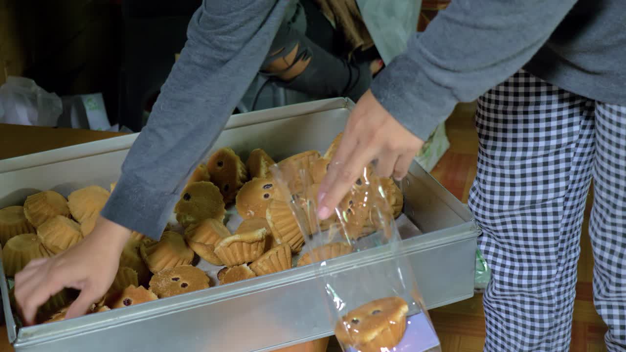 manos de mujer poniendo pastelitos tailandeses tradicionales con pasas en una bolsa de plástico transparente