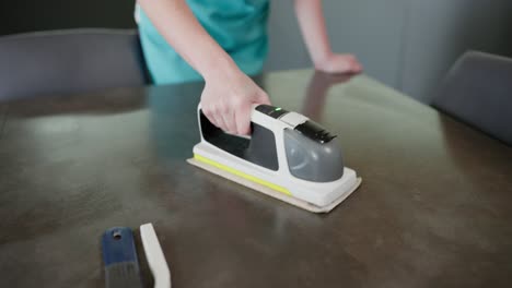 Close-up-a-girl-in-a-blue-apron-polishes-the-surface-of-a-glossy-table-in-the-kitchen-using-a-device-for-cleaning-an-apartment-and-kitchen