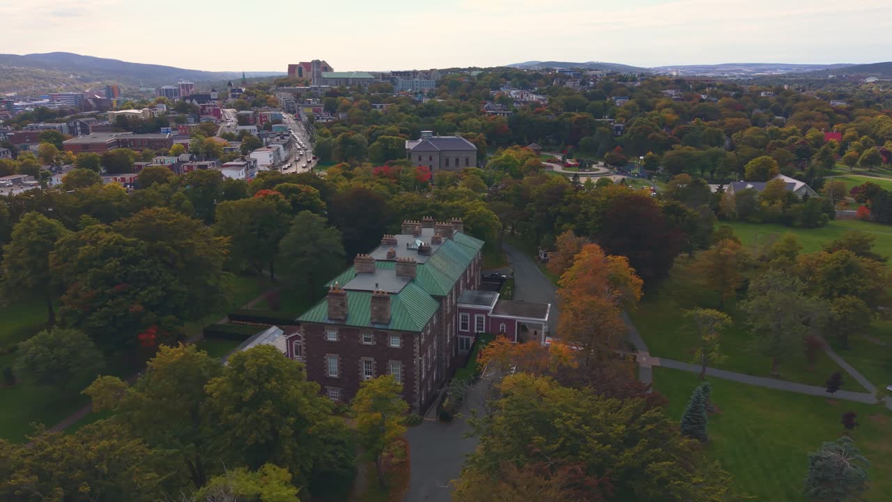 A high altitude drone flight over St. John's Newfoundland in autumn reveals rolling forested hills painted in vibrant hues, with the distant city skyline and harbour glistening under clear skies