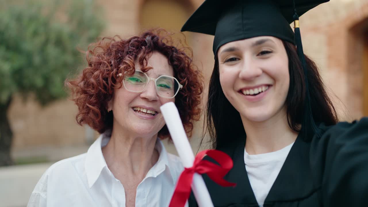 Two women mother and daughter holding graduate diploma having video call at campus university