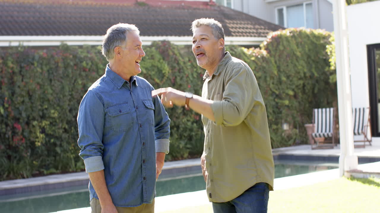 Amigos mayores conversando y riendo juntos al aire libre cerca de una piscina.