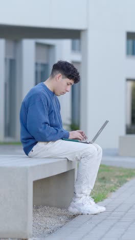 young student working on laptop outside university building. vertical
