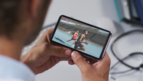 Composite-of-male-doctor-watching-athletics-running-event-on-smartphone