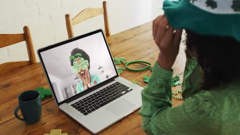 mujer afroamericana sonriente que usa artículos en forma de trébol en una videollamada en una computadora portátil