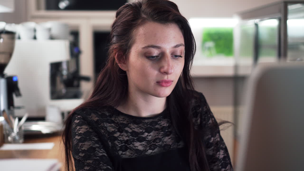 Girl face looking into computer screen at reception, coffee machine in background, closeup view