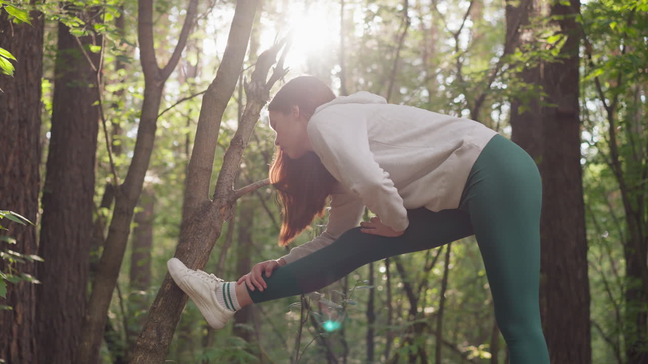 joven se estira para calentarse en el bosque. mujer se prepara antes de ir a correr en la mañana de verano rodeada de árboles. rutina activa para el bienestar