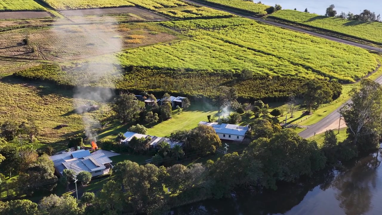 Luftperspektiv bevæger sig hen over en australsk farm med røg, der stiger op nær en flodbred