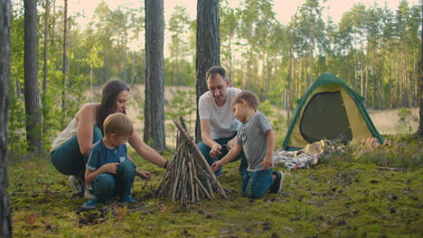 Die-Familie-Sitzt-An-Einem-Sommerabend-Am-Lagerfeuer.-Kinder-Ruhen-Sich-Mit-Ihren-Eltern-Im-Wald-Aus.-Wochenende-In-Der-Natur-In-Guter-Gesellschaft.-Familie-Brät-Würstchen-über-Einem-Feuer-Im-Wald.