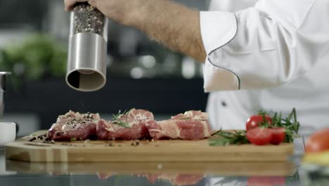 Male-chef-peppering-meat-at-kitchen.-Closeup-chef-hands-peppering-steak