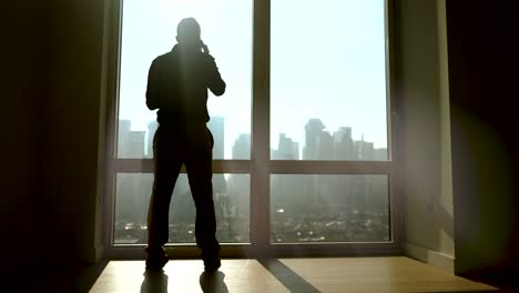 outlines of man opening blinds on big windows. sun shines into the room, producing shadows.